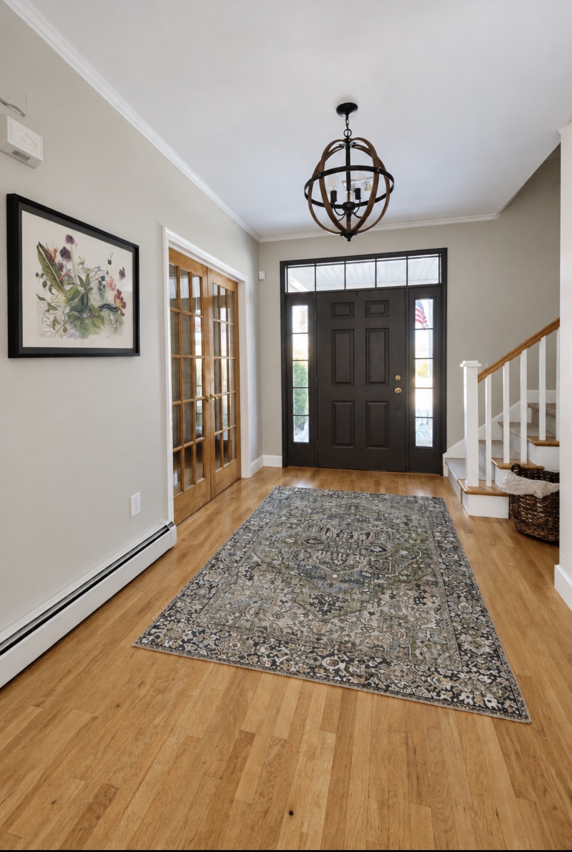 Entryway with black front door, botanical art, warm wood floor and muted green patterned runner
